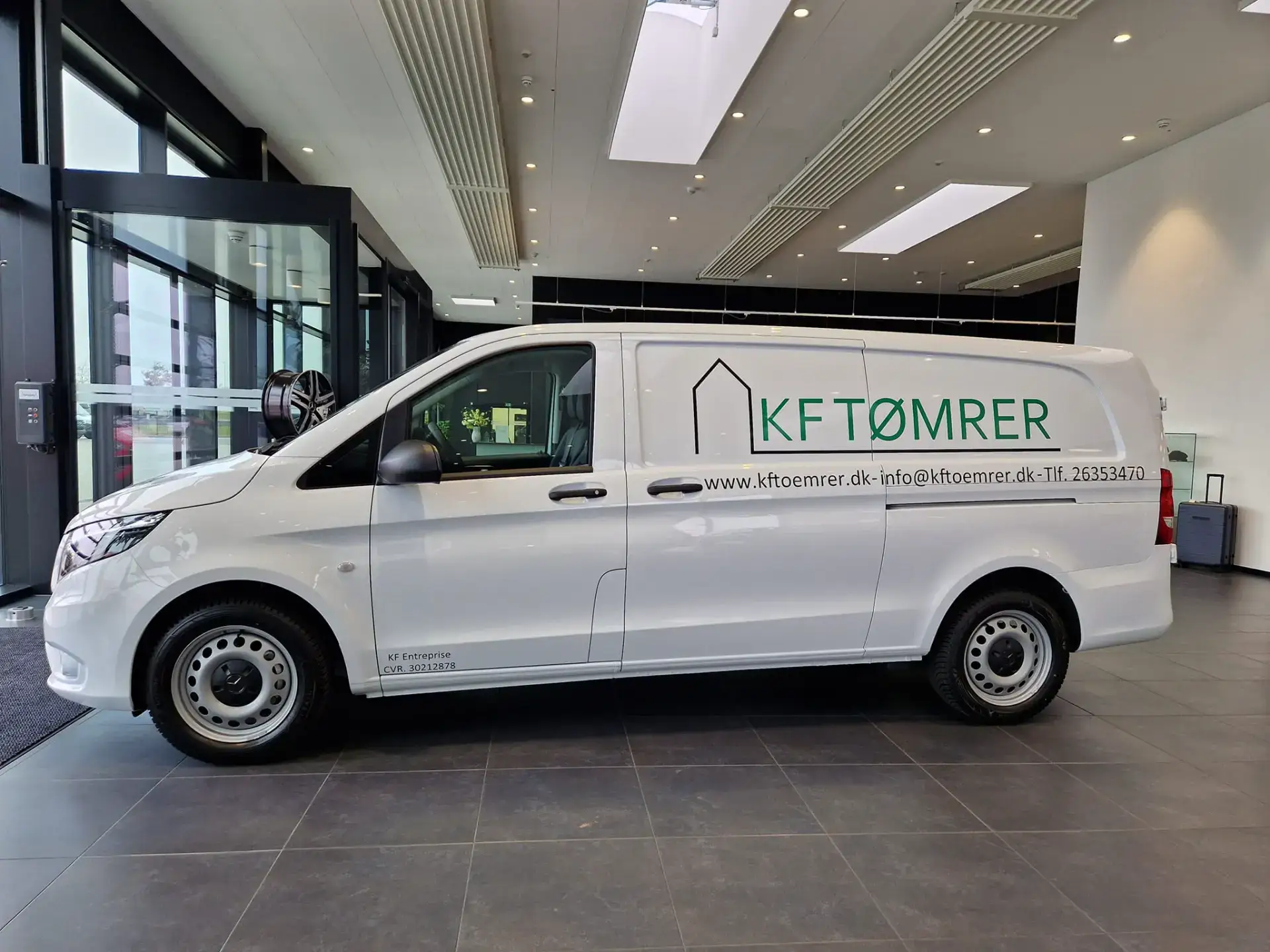 KFTømrer firmabil med logo, klar til serviceopgaver, parkeret indendørs i moderne showroom.