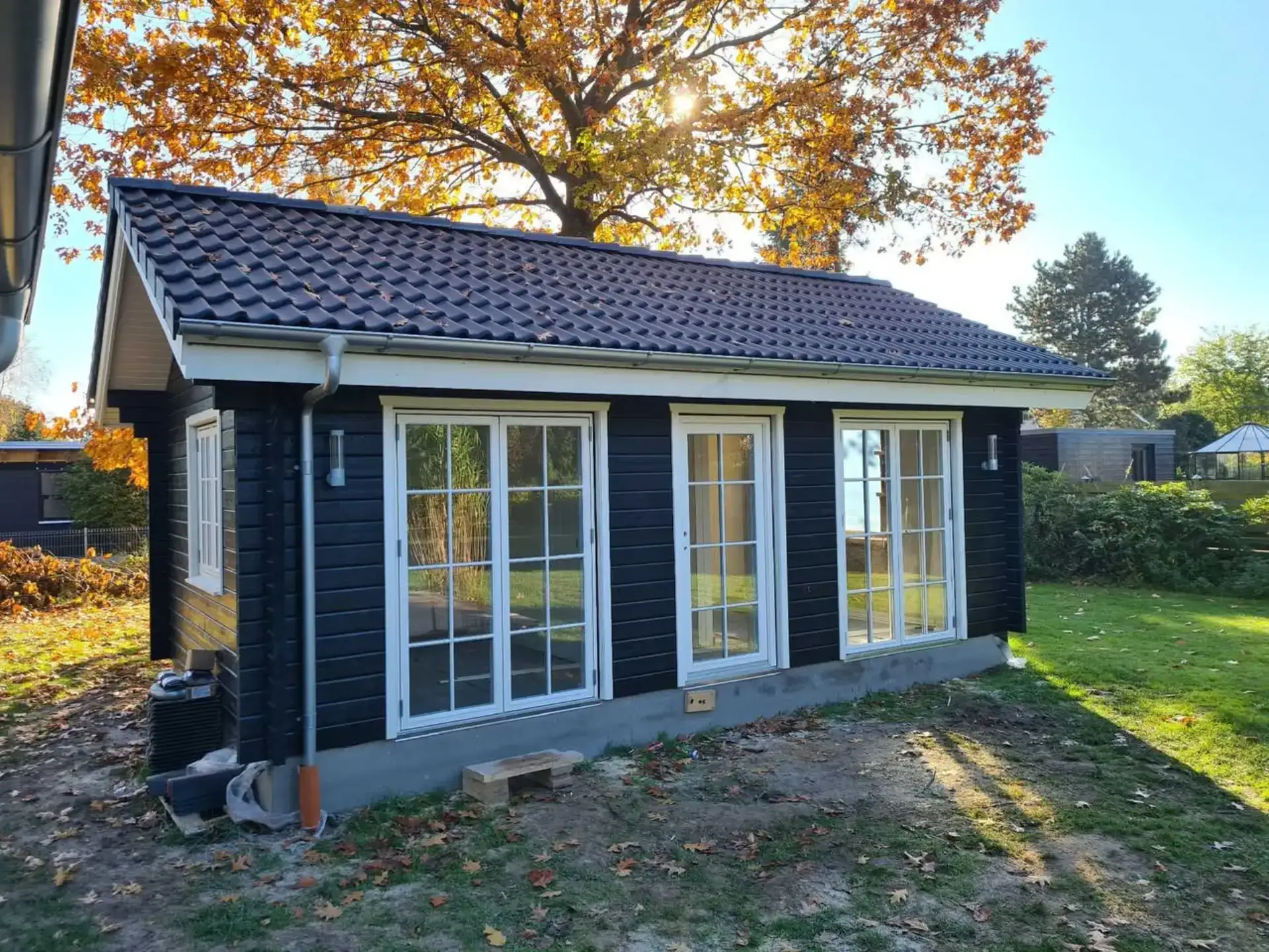 Hus med store glasdøre, sort træfacade og tag i teglsten, ideelt til udendørs ophold og havebrug.